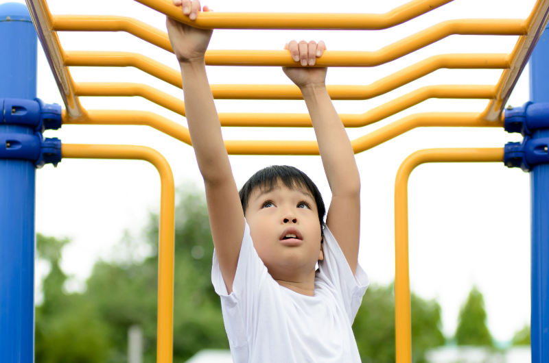 young-asian-boy-hang-the-yellow-bar-by-his-hand-to-exercise-at-out-door-playground