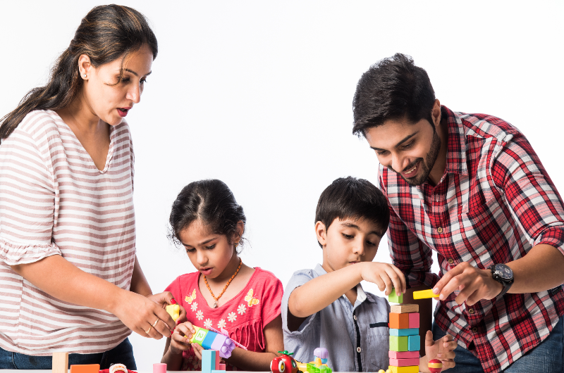 indian-small-kids-playing-colourful-block-toys-with-young-parents-against-white-background