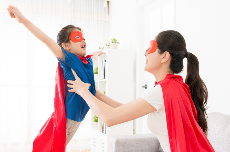 pretty-young-mother-holding-cute-little-girl-making-fly-posing-and-playing-as-superhero-at-home